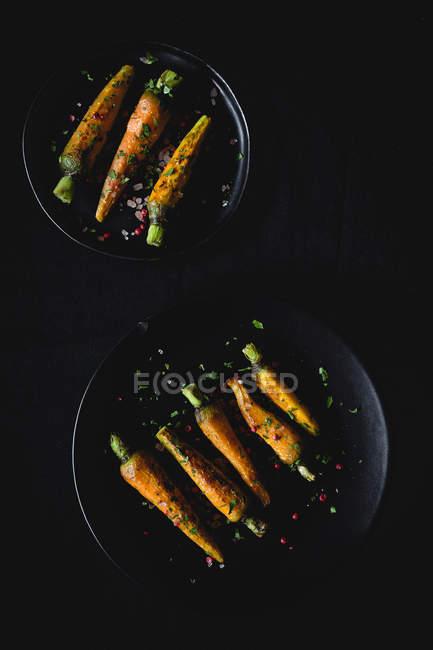 Carote arrosto sane con erbe e spezie su piatti neri su sfondo scuro — Foto stock