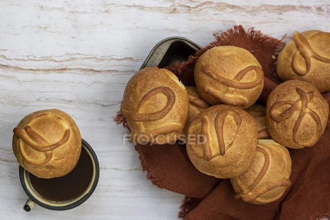 Fresh baked buns in heap on brown napkin on wooden table with cup of tea — Stock Photo