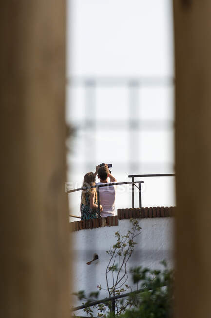 Vista trasera de una pareja irreconocible parada en el techo y tomando selfie con cámara fotográfica - foto de stock