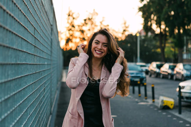 Весела молода жінка, що йде по вулиці біля автомобілів на заході сонця — стокове фото