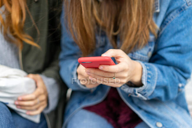 Mulher de corte segurando telefone celular vermelho e sentada perto de senhora em roupas casuais no Porto, Portugal — Fotografia de Stock