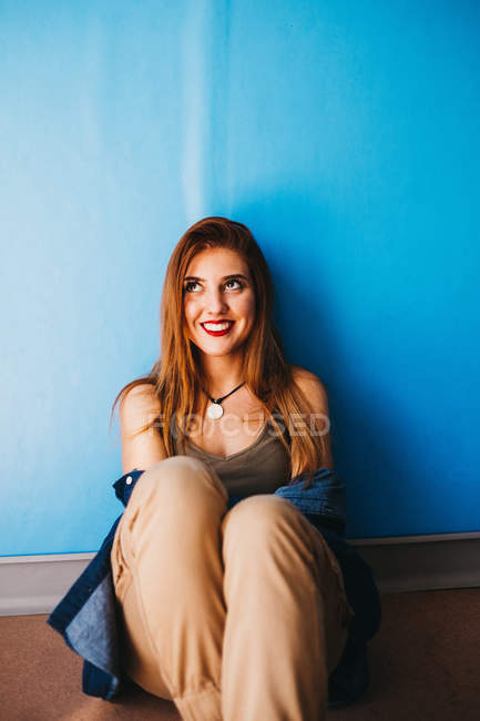 Приваблива жінка сидить біля синьої стіни — стокове фото