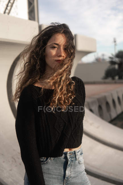 Bella giovane donna con i capelli ricci in piedi su sfondo sfocato della strada della città — Foto stock