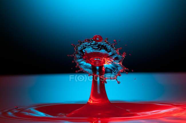 Closeup tiro de respingo de líquido transparente de cor no fundo azul — Fotografia de Stock