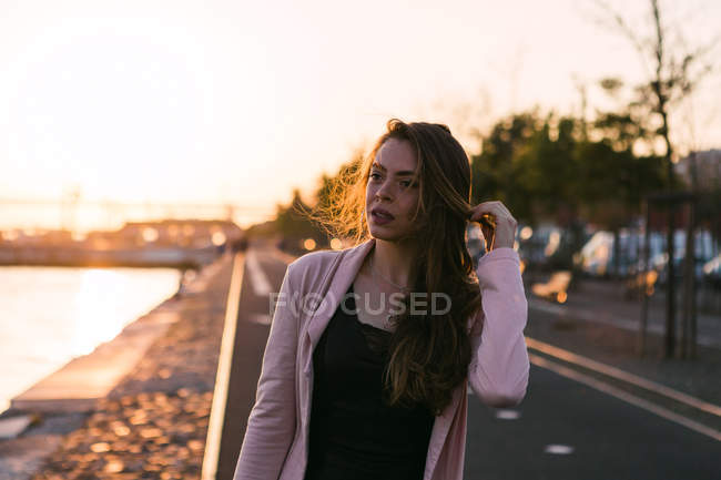 Молода дівчина з рукою в волоссі, що йде по алеї на заході сонця — стокове фото