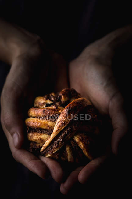 Close-up of human hands holding small chocolate bun on dark background — Stock Photo