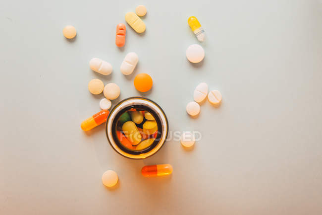 Різнокольорові таблетки та капсули розкидані та коробка для таблеток на білому тлі — стокове фото