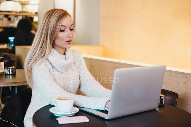 Senhora usando laptop na mesa com xícara de bebida e smartphone — Fotografia de Stock