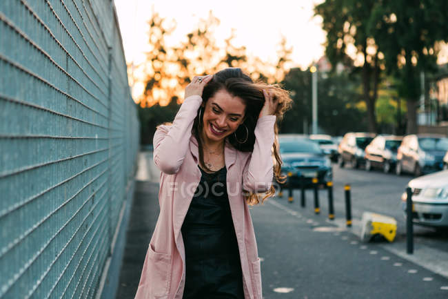 Riendo joven mujer caminando en la calle cerca de los coches al atardecer - foto de stock