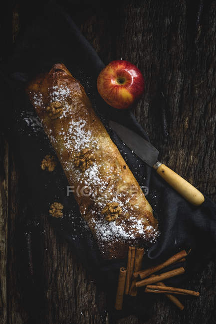 Домашний яблочный штрудель с орехами, изюмом и корицей на фоне темного дерева — стоковое фото