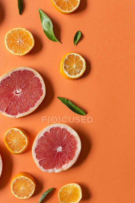 Шматочки мандарина і грейпфрута з зеленим листям на помаранчевому фоні — стокове фото