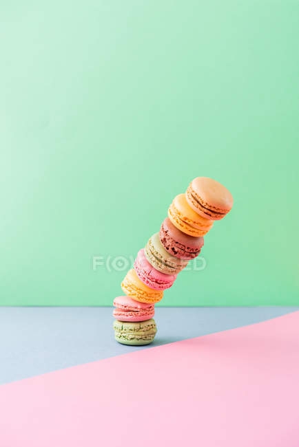 Falling pile of fresh tasty macarons on blue board on green background — Stock Photo