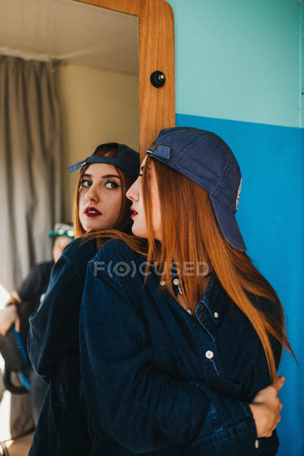 Jovem encantadora mulher de cabelos vermelhos em desgaste casual com a mão cruzada olhando para reflexão perto da parede azul — Fotografia de Stock