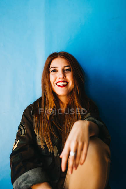 Femme attrayante souriante assise dans un mur bleu — Photo de stock
