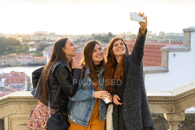 Привабливі усміхнені жінки у повсякденному одязі роблять селфі на смартфоні на задньому плані в Порту (Португалія). — стокове фото