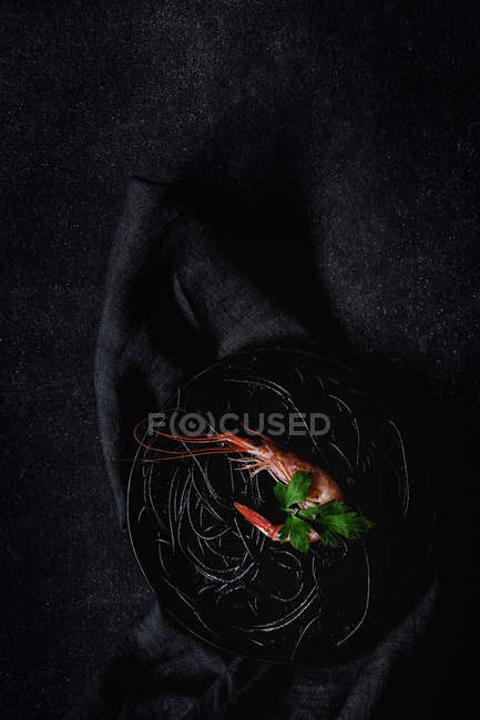 Schwarze Nudeln mit Garnelen auf schwarzem Teller — Stockfoto