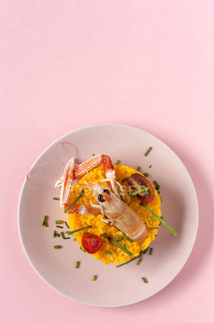 Paella caseira com lagostins e camarões no prato no fundo rosa — Fotografia de Stock