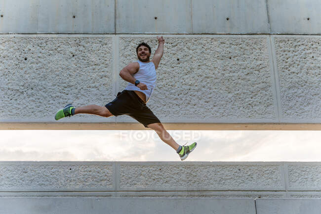 Привлекательный бородатый мужчина в спортивной одежде улыбается и прыгает высоко во время тренировок на улице — стоковое фото
