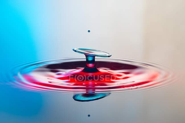 Closeup tiro de respingo de líquido transparente colorido no fundo colorido — Fotografia de Stock