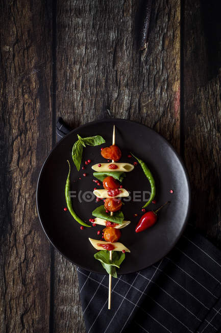 Macaroni with tomato and basil on stick on black plate with sauce on dark wood — Stock Photo