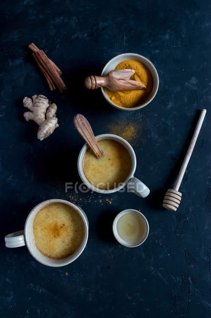 Bols avec des épices et des tasses de latte épicé dans des tasses sur fond sombre — Photo de stock