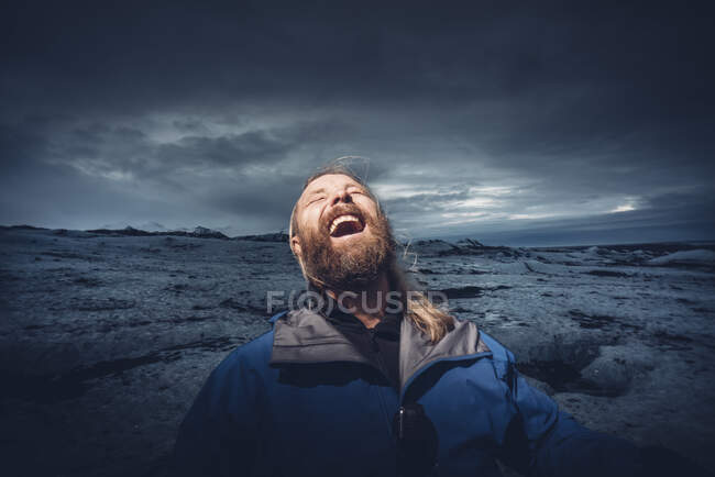 Barbudo hombre excitado gritando de felicidad en el punto de luz al aire libre en un amplio terreno frío, Islandia - foto de stock