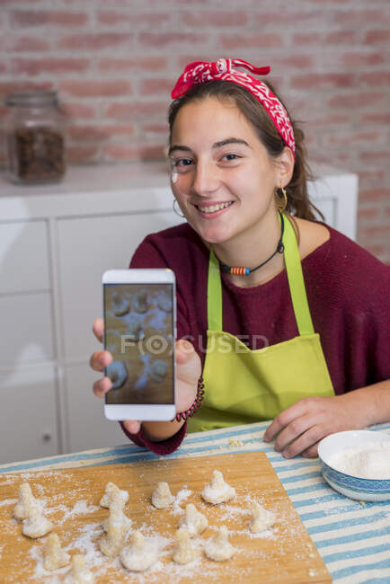 Дівчина-підліток використовує смартфон під час роботи над традиційною випічкою — стокове фото