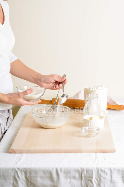 Ritagliato di donna versando zucchero nella ciotola durante la cottura in cucina . — Foto stock