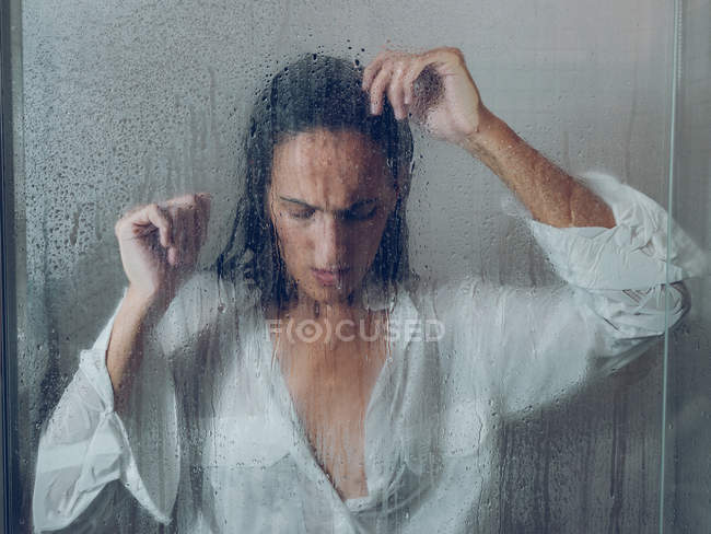 Attraente giovane signora in camicia bianca bagnata in piedi vicino al vetro della cabina doccia — Foto stock