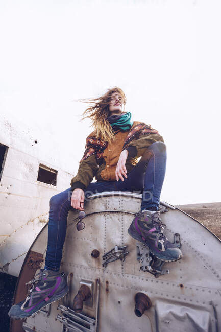 Молода жінка в теплому одязі сидить на розбитому літаку між темними просторами Ісландії. — стокове фото