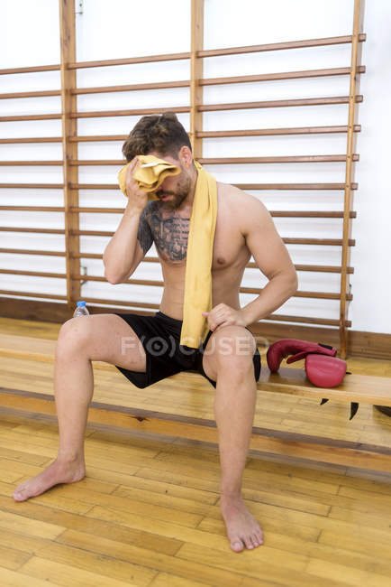 Втомлений м'язовий спортсмен з рушником відпочиває після тренування на лавці в спортзалі — стокове фото
