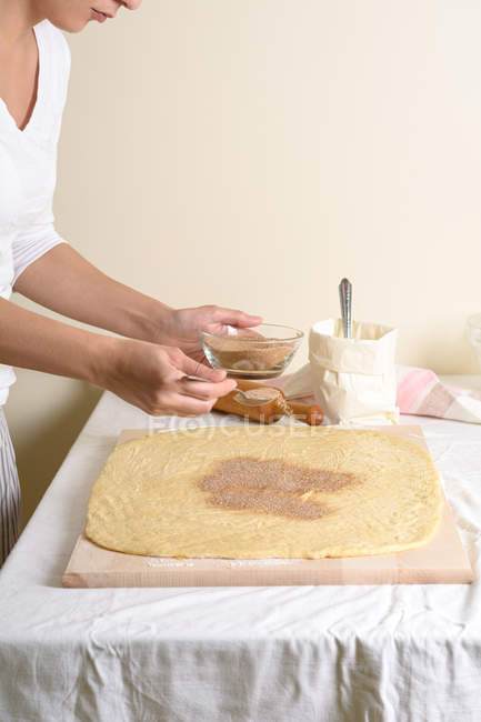 Cropped of woman putting cinnamon in dough in kitchen. — Stock Photo