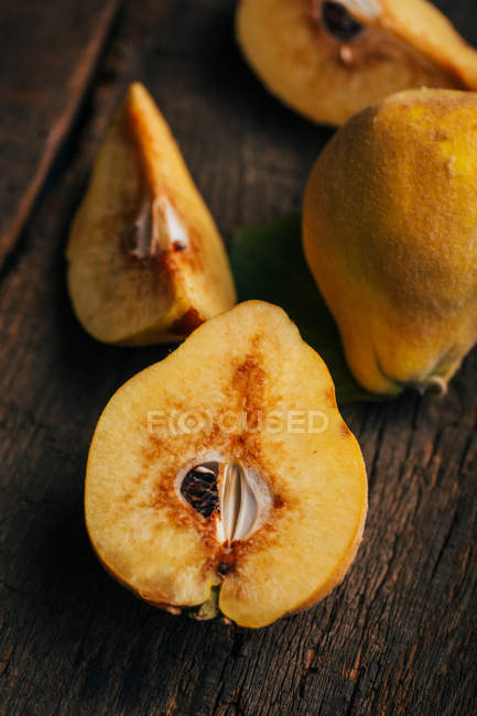 Whole and halved quinces on dark wooden background — Stock Photo