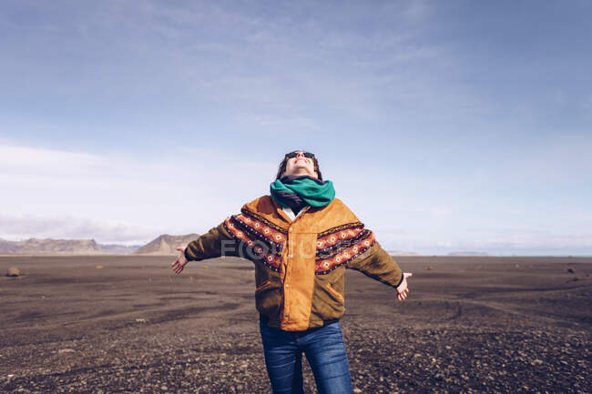 Smiling human with upping head and hands to sides standing between dark grounds in Iceland — Stock Photo