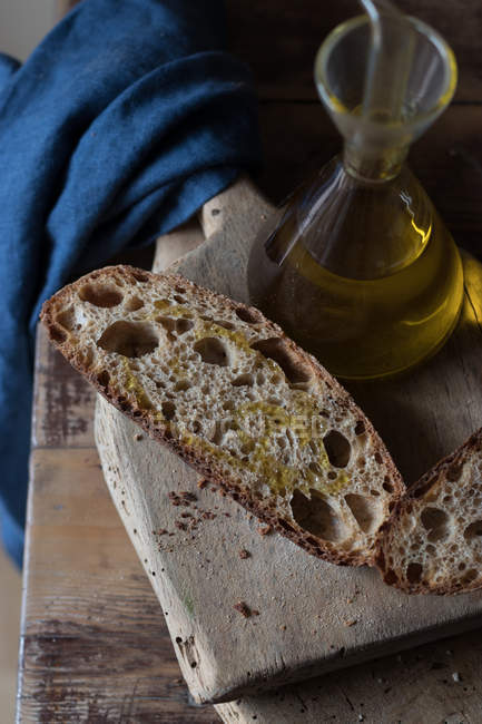 Slices of wholemeal bread on rustic wooden chopping board with bottle of oil — Stock Photo