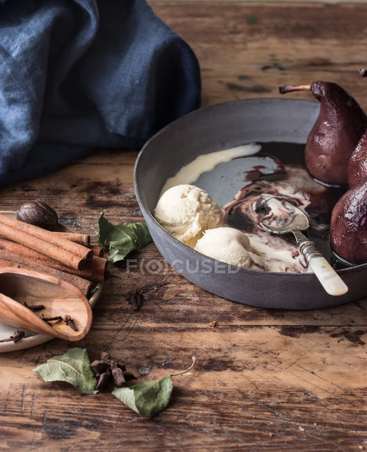 Aromatic cinnamon sticks on wooden tabletop near bowl with melting ice cream and delectable mulled pears in wine — Fotografia de Stock