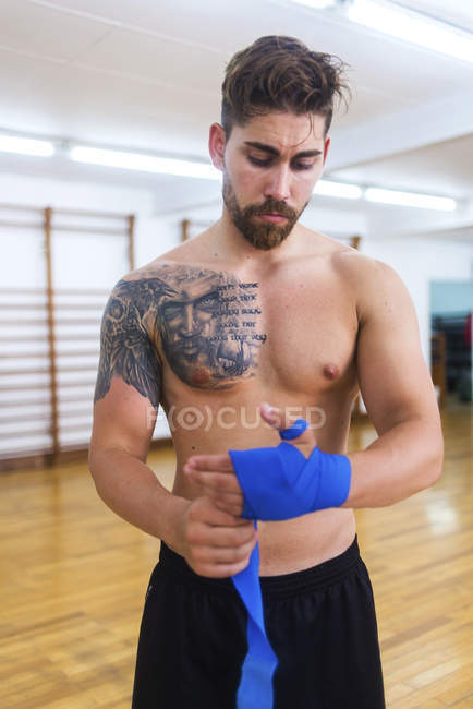 Young boxer wrapping hands before training in gym — Stock Photo