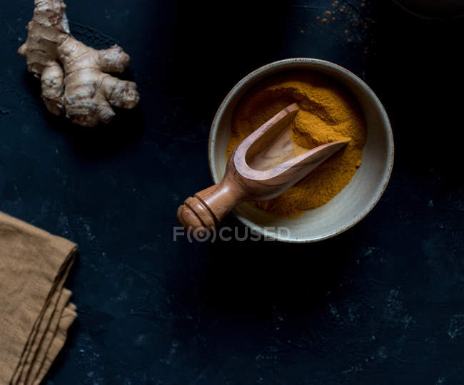 Bol avec curcuma séché et racine de gingembre frais sur fond sombre — Photo de stock
