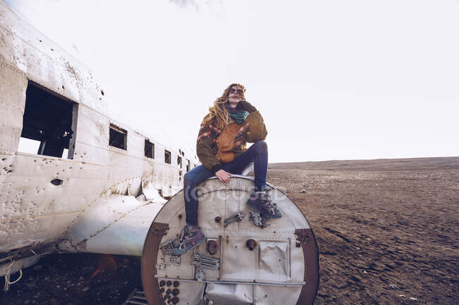 Молода жінка в теплому одязі сидить на розбитому літаку між темними просторами Ісландії. — стокове фото