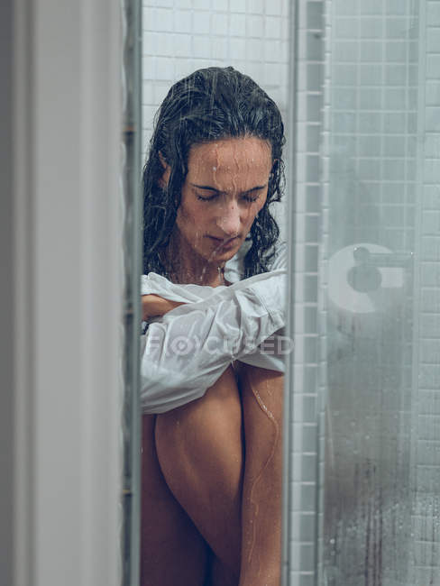 Esguichando triste jovem mulher na camisa sentado no chuveiro — Fotografia de Stock