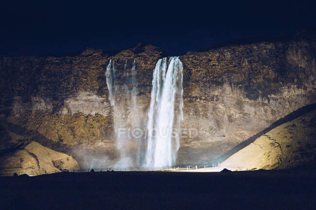Beleuchtete Wasserkaskade stürzt in der Dunkelheit in Island zwischen Felsen — Stockfoto