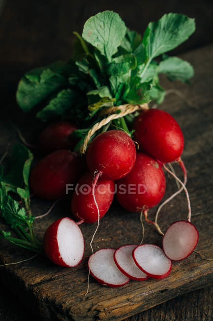 Bouquet de radis frais et tranches sur fond de bois — Photo de stock