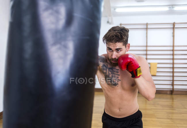 Young bearded guy training in gym with punch bag — Stock Photo