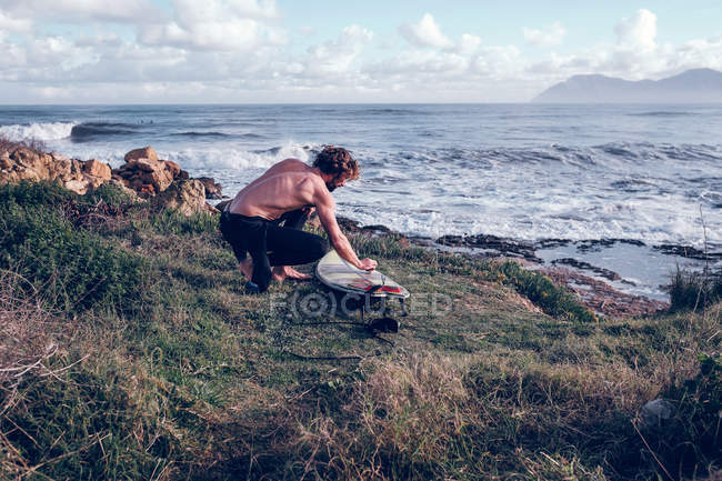 Jovem limpando prancha na costa oceânica — Fotografia de Stock