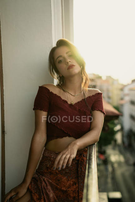 Retrato de la encantadora joven morena de pie en el balcón con retroiluminación - foto de stock