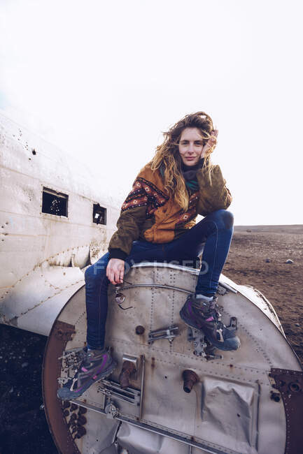 Jovem senhora no desgaste quente sentado em aeronaves quebradas entre terrenos escuros na Islândia — Fotografia de Stock