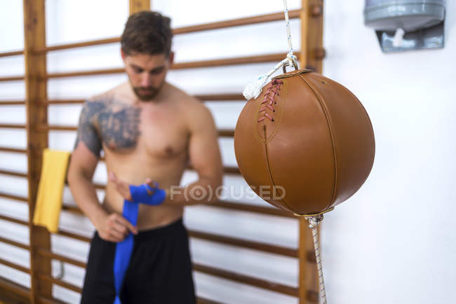 Saco de soco no ginásio e jovens boxeadores que embrulham as mãos no fundo — Fotografia de Stock