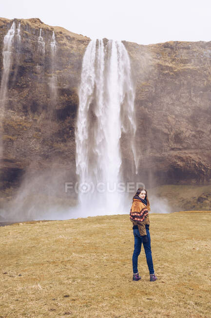 Voltar vista jovem senhora no campo perto de cascata de água caindo no rio entre rochas na Islândia — Fotografia de Stock