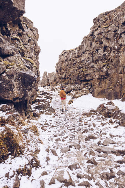 Junger Mann geht in Schlucht mit Schnee zwischen Steinhügeln in Island — Stockfoto