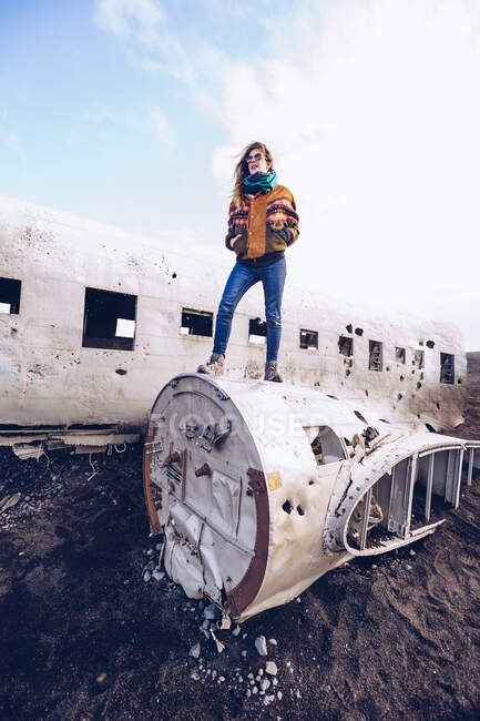 Молода жінка в теплому одязі на розбитому літаку між темними просторами в Ісландії. — стокове фото